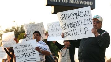 Residentes protestan frente a la estación de Policía de Maywood. Piden en sus pancartas ayuda al gobernador.