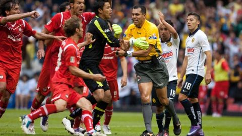 Jugadores del Toluca se abalanzan sobre el árbitro Erim Ramírez para reclamarle luego de que éste marcara una mano de Diego Novaretti.
