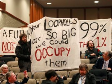 Miembros de 'Ocupemos Albany' sostienen pancartas durante una audiencia sobre el presupuesto ayer en Albany, NY.