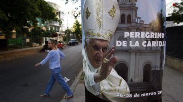 Una mujer camina junto a un cartel con la imagen del Papa Benedicto XVI, en La Habana (Cuba) a pocos días antes del inicio de la visita del sumo pontífice a la isla.