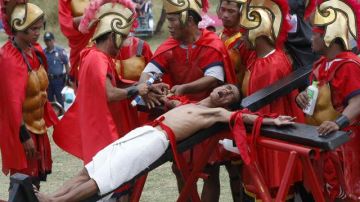 Voluntarios vestidos como Centuriones Romanos, clavan en una cruz de madera la mano un identificado devoto durante el Viernes Santo en Filipinas.