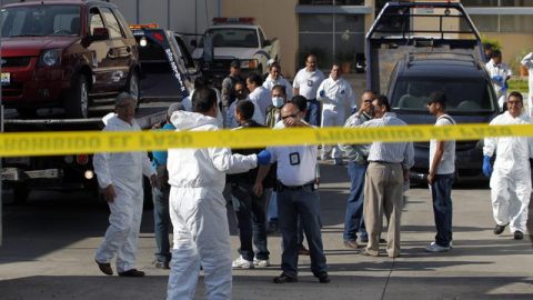 Expertos forenses revisan los dos vehículos donde fueron hallados los cuerpos de once personas, en una carretera.