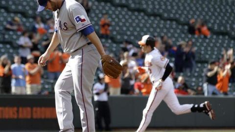 Colby Lewis (izq.), de los Rangers disimula después de recibir un jonrón de Ryan Flaherty, quien (al fondo) recorre las bases.