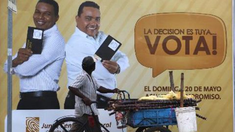 Un vendedor de caña de azúcar camina  cerca de una propaganda electoral.