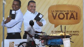 Un vendedor de caña de azúcar camina  cerca de una propaganda electoral.