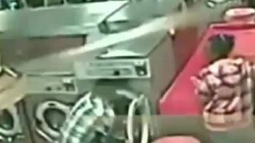 Imagen tomada del video de una cámara de seguridad en la que se ve al padre metiendo a su hijo dentro de la lavadora.