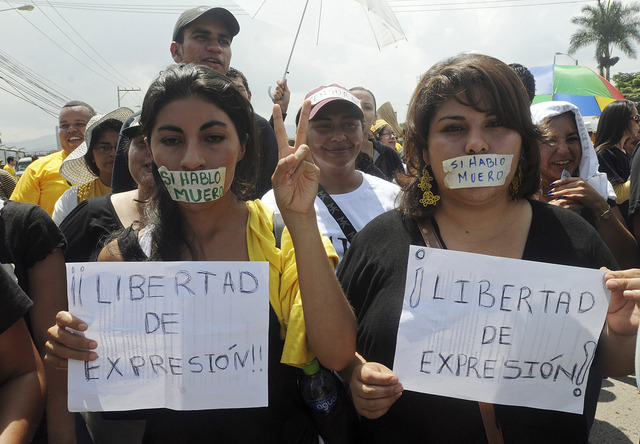 Periodistas y manifestantes marchan con la boca tapada con una cinta en la que se lee en español "Si hablo me muero" y pancartas que rezan "Libertad de expresión!" durante  una protesta en contra la violencia.