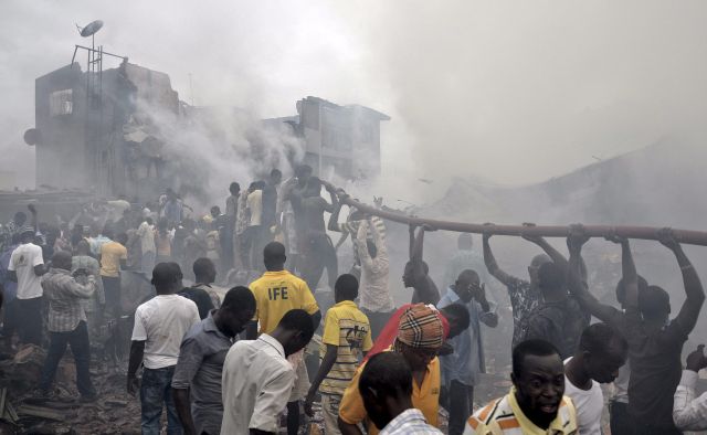 Nigerianos ayudan a sostener una manguera para apagar las llamas en el lugar donde quedaron los escombros de un avión comercial que se estrelló con 159 personas a bordo en Lagos, Nigeria.
