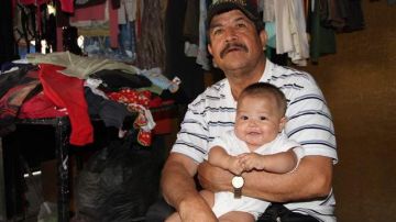 Lucio González carga a su nieto en la tienda de ropa de segunda mano que abrió a su regreso de EEUU.