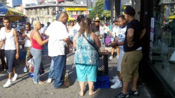 Apostadores rodean al hombre en su improvisada mesita de juegos de azar en East Fordham Road, El Bronx.