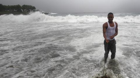 Un hombre pasea con su perro en el mar donde se registra fuerte oleaje por el paso de la tormenta tropical Ernesto ayer.