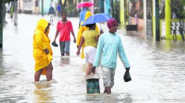 Varias personas caminan por una calle inundada en Jaquimeyes (República Dominicana), tras el paso de la tormenta "Isaac".