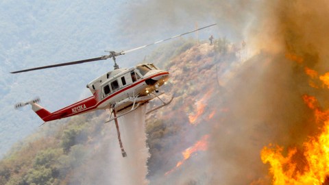 Helicópteros especiales de rescate  lanzan agua y  espuma para apagar las llamas del fuego forestal.
