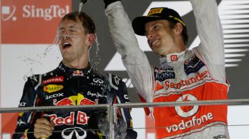 El británico Jenson Button  (izq.), segundo en Singapur, baña en champaña al ganador de la prueba de la Fórmula Uno, el alemán  Sebastian Vettel.
