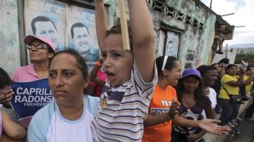 Una mujer  y su hijo esperan la llegada del candidato presidencial opositor Henrique Capriles durante un acto de campaña ayer en Miranda, Venezuela, mientras en la pared fueron fijads afiches del presidente Hugo Chávez.