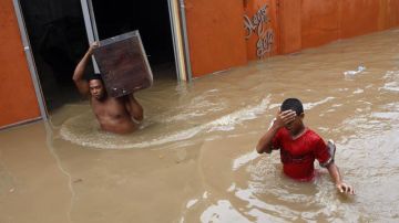 Dos personas abandonan sus hogares en el barrio La Barquita, en Santo Domingo (República Dominicana), una de las zonas más afectadas por 'Sandy'.