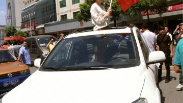 Una mujer con una bandera china pide a protestantes no atacar su carro toyota durante una manifestacion contra la compañía de autos en ese país.