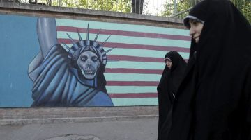 Estudiantes iraníes pasan junto a una pared pintada contra los Estados Unidos.