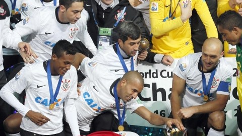 El peruano Paolo Guerrero posa envuelto en una bandera de su país, mientras sus compañeros del Corinthians admiran el trofeo de campeones mundiales.