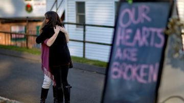 Dos residentes de Newtown se abrazan tras la matanza ocurrida en una escuela de la zona. A la derecha un letrero que dice "Nuestros corazones están rotos".
