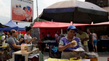 Una vendedora   ofrece sus productos en un mercado callejero próximo a un póster que invita a votar por el candidato de la oposición, Henrique Capriles.