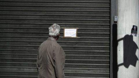 Una persona observa un cartel colocado en una sucursal cerrada del Banco Popular chipriota en las calles de Atenas, Grecia.