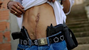 Joan, un delincuente y vendedor de drogas apodado "El Patan", muestra dos de las armas que lleva consigo en un barrio de Caracas.