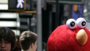 Un personaje de Elmo utiliza una cámara de una cliente para fotografiarla con un compañero que interpreta a “Cookie Monster” en la zona de Times Square.