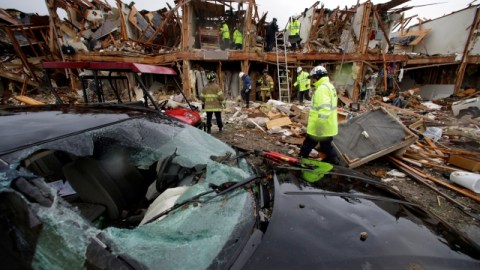 Un coche severamente dañado se observa enfrente de un edifico de departamentos totalmente destruído como resultado de la explosión mientras rescatistas inspeccionan el lugar en West, Texas.