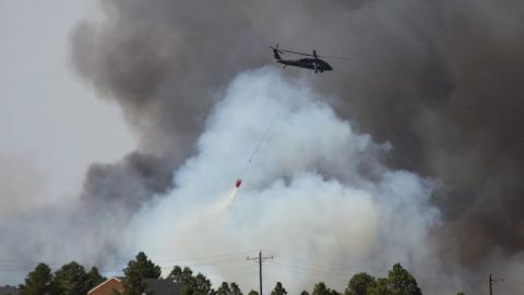Un helicóptero descarga agua en un intento de detener las llamas que han destruido más de 90 casas y obligado la evacuacón de miles de residentes de la zona.