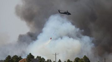 Un helicóptero descarga agua en un intento de detener las llamas que han destruido más de 90 casas y obligado la evacuacón de miles de residentes de la zona.