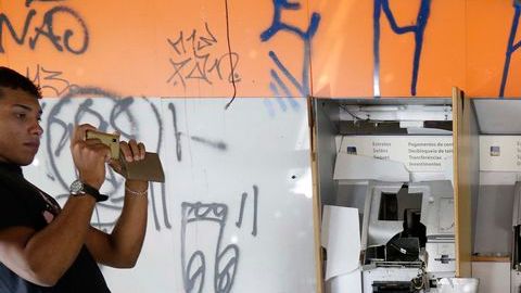 Un hombre toma fotos de una sucursal bancaria completamente destrozada durante los disturbios de anoche en Sao Paulo.