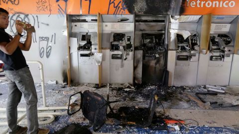 Un hombre toma fotos de una sucursal bancaria completamente destrozada durante los disturbios de anoche en Sao Paulo.