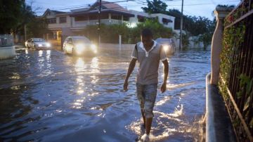 Un hombre camina por una calle inundada horas antes de la llegada de la tormenta tropical "Chantal" a Santo Domingo.