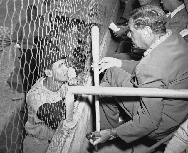 En esta histórica foto, Ted Williams dialoga con Babe Ruth quien examina un bate y  disfruta de un momento en la tribuna.