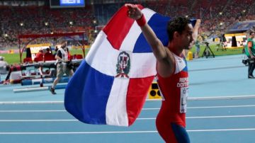 El dominicano Luguelin Santos celebra con la bandera de su país tras ganar el bronce en los 400 metros del Mundial de Atletismo.