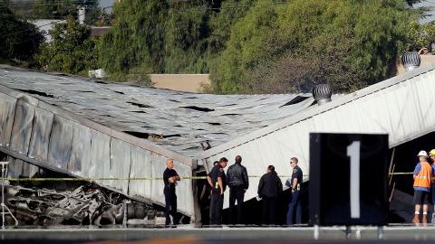 Autoridades del aeropuerto e investigadores frente al hangar que se derrumbó al estrellar una avioneta en el aeropuerto de Santa Monica el domingo por la noche. Los investigadores esperaban la llegada de una grúa el lunes para poder llegar al avión, enterrado por el derrumbe.