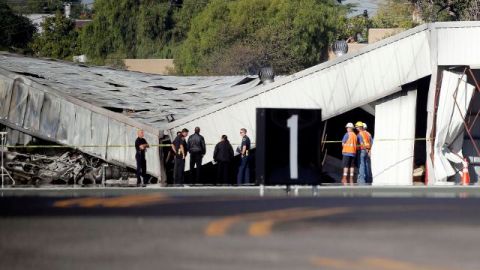 Autoridades del aeropuerto e investigadores frente al hangar que se derrumbó al estrellar una avioneta en el aeropuerto de Santa Monica el domingo por la noche. Los investigadores esperaban la llegada de una grúa el lunes para poder llegar al avión, enterrado por el derrumbe.