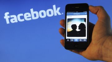 Una persona porta un iPhone4 de Apple con la aplicación de Instagram abierta en el dispositivo, frente al logo de Facebook.