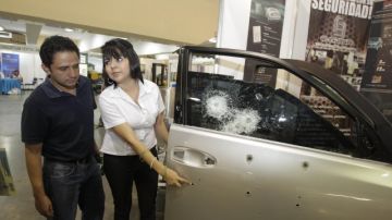 Una expositora de la empresa Blindasal  enseña la ventanilla de un carro blindado que recibió impactos de bala, que no penetraron totalmente.