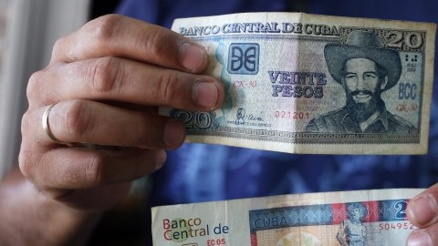 Un hombre muestra billetes cubanos de veinte pesos, uno de CUP (arriba) y otro de CUC (abajo).