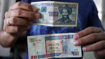 Un hombre muestra billetes cubanos de veinte pesos, uno de CUP (arriba) y otro de CUC (abajo).