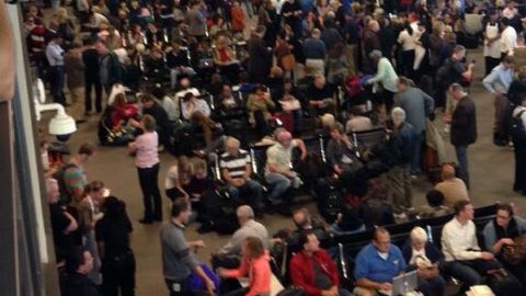 Pasajeros esperan en la Terminal Internacional Tom Bradley del Aeropuerto Internacional de Los Ángeles, donde miles de vuelos están retrasados después de un tiroteo.