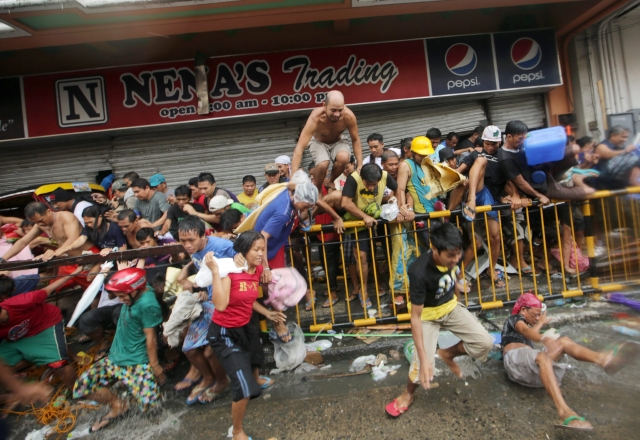 Filipinos corren tras salir de una tienda de abarrotes que fue saqueada por un grupo de personas en Taclobán.