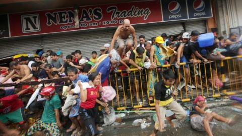 Filipinos corren tras salir de una tienda de abarrotes que fue saqueada por un grupo de personas en Taclobán.