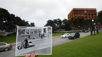 En primer plano, foto del 22 de noviembre de 1963 que muestra a ciudadanos agachados en la Plaza Dealey (también de fondo), mientras un policía transita en una moto poco después del tiroteo al presidente Kennedy.