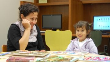 Una madre latina ayuda a su hija de preescolar a comprender el concepto de correspondencia en una biblioteca pública.