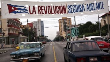 Varios autos circulan  por una céntrica avenida bajo un cartel alusivo a la revolución cubana en La Habana, Cuba.