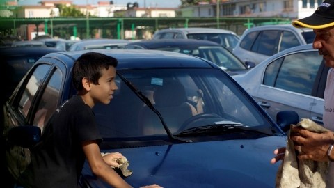 Un trabajador de la concesionaria de automóviles, a la derecha, y un niño  limpia un Geely chino usado para la venta en un concesionario del Gobierno en La Habana.