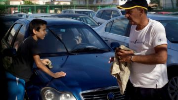 Un trabajador de la concesionaria de automóviles, a la derecha, y un niño  limpia un Geely chino usado para la venta en un concesionario del Gobierno en La Habana.